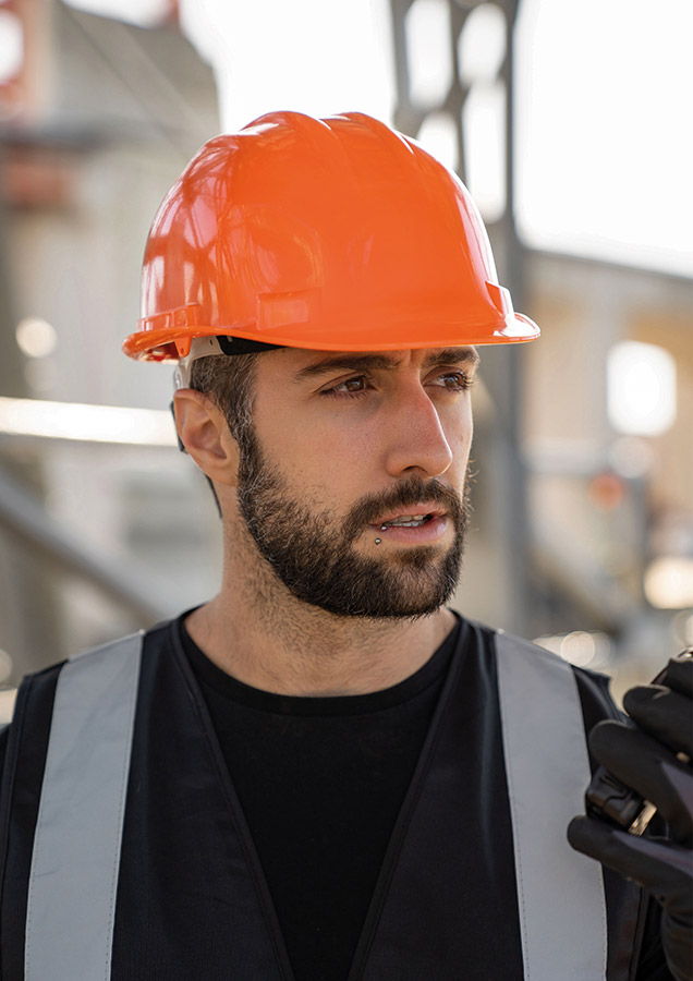 Adult construction worker wearing an orange-coloured Korntex safety helmet on a construction site