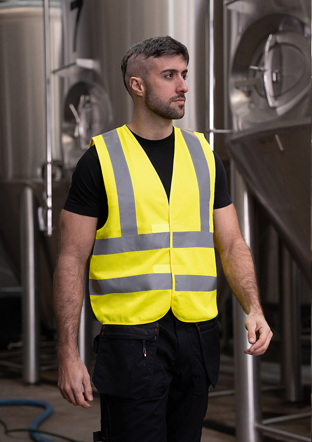 Adult man in fluorescent signal yellow Korntex safety vest standing in front of large metal containers