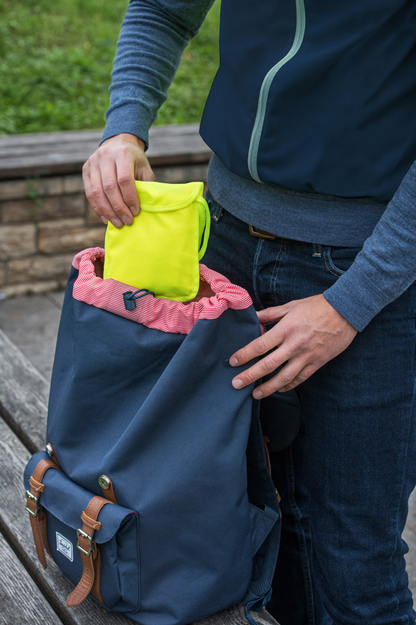 Adult stows yellow safety vest in a blue rucksack