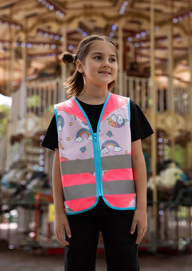 Child in a neon pink Korntex safety vest with a unicorn pattern in front of a children's carousel