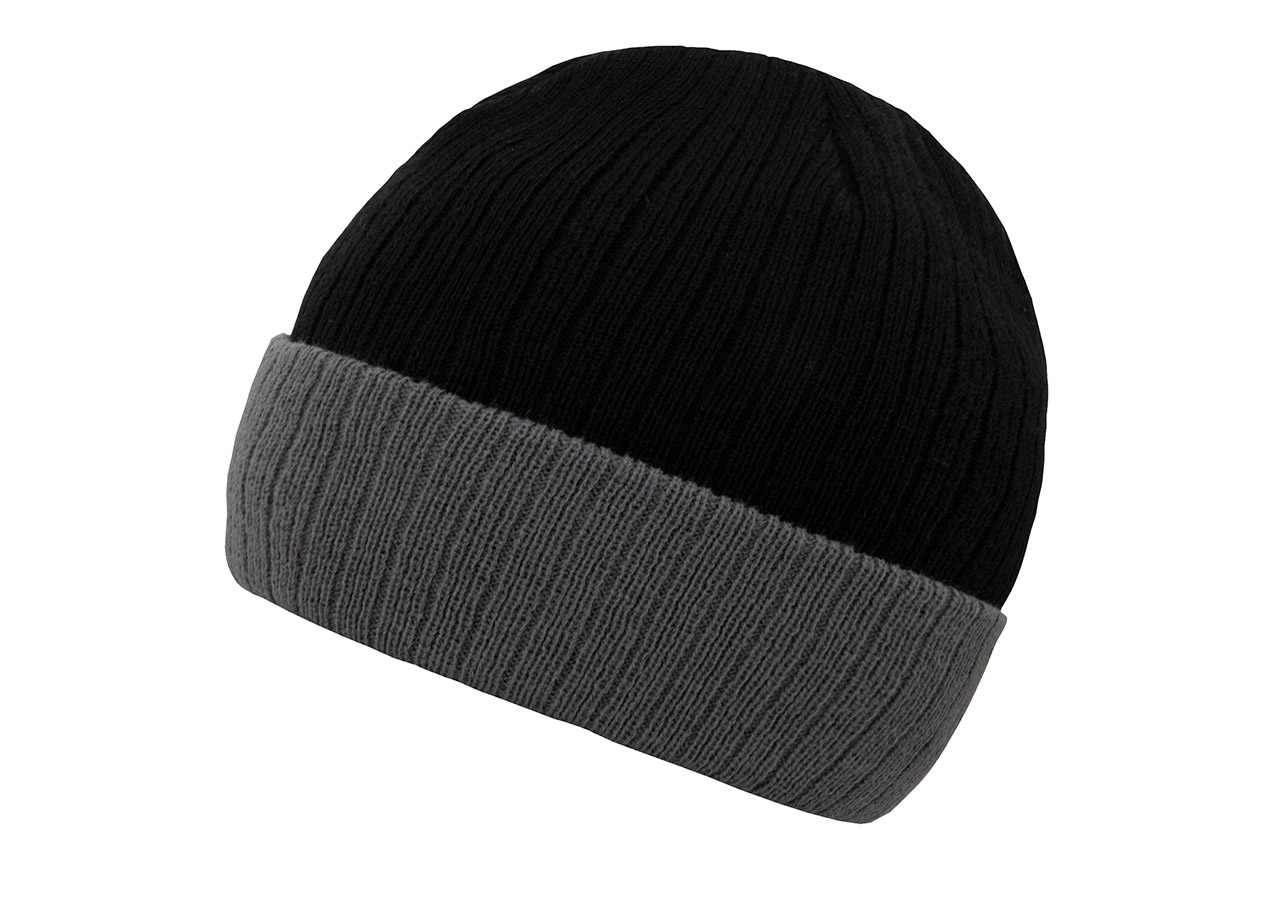 An adult wears an embroidered, black and grey Korntex knitted hat in front of a grey wall