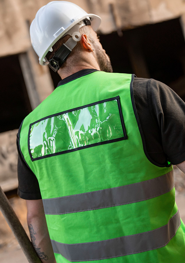 A man is wearing a green Korntex safety vest and the black Korntex ID pocket with transparent field of vision can be seen on the back