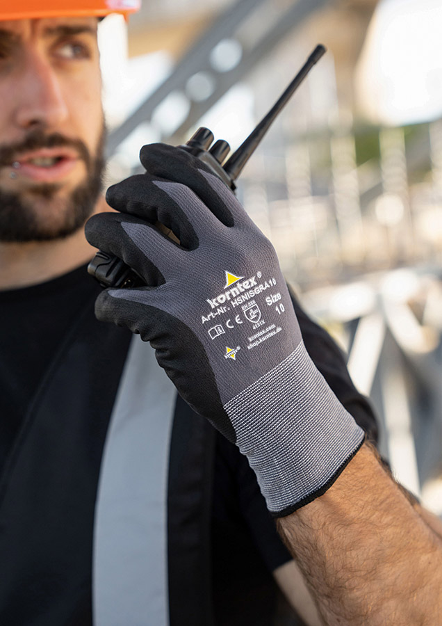 A man with grey-black Korntex gloves holds a walkie-talkie