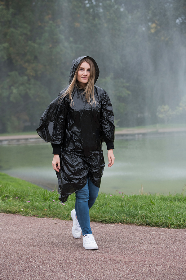Adult woman wearing a black Korntex disposable raining poncho in a park