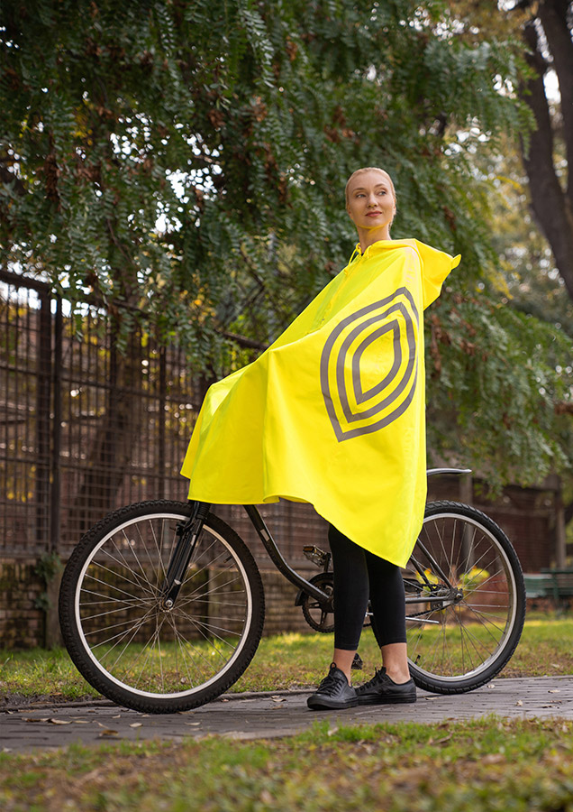 Woman wearing a yellow hooded rain poncho while standing next to a bicycle on a cycle path
