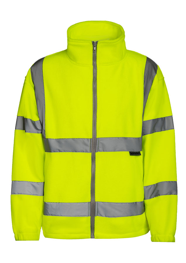 Adult man wearing a signal orange Korntex hi-vis fleece jacket with reflective stripes walking in front of an industrial buil