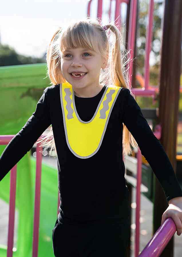 A child wearing a yellow Korntex multi-use collar with reflective strips is standing in a park.