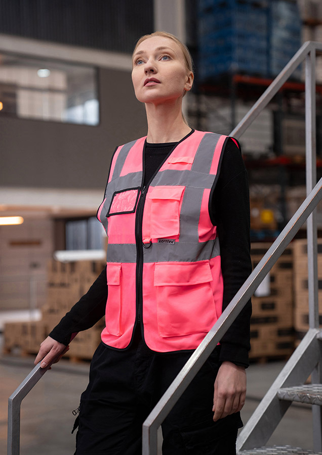 A woman wears a pink Korntex safety vest with reflective stripes in a warehouse