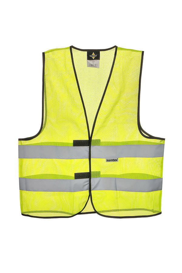 Adult construction worker stands on a building site in a yellow Korntex mesh safety vest and yellow helmet holding tools