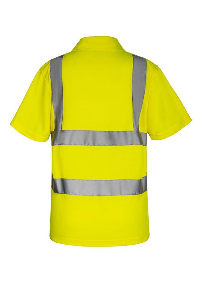 An adult construction worker is standing in front of a demolished building, wearing a fluorescent yellow Korntex polo shirt with a walkie-talkie.