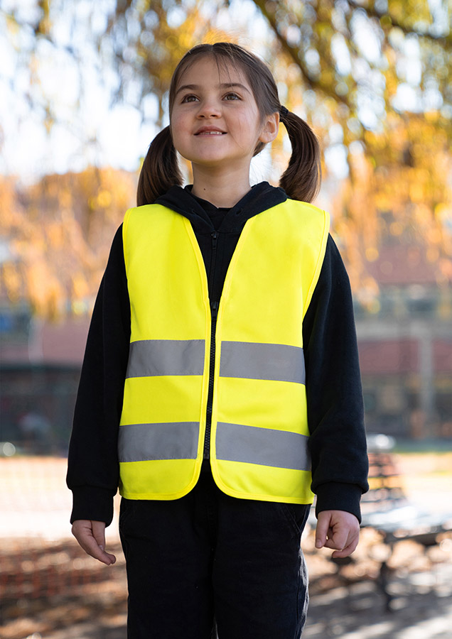 Young smiling girl in signal yellow Korntex safety vest with reflective stripes and zip fastener standing in the park