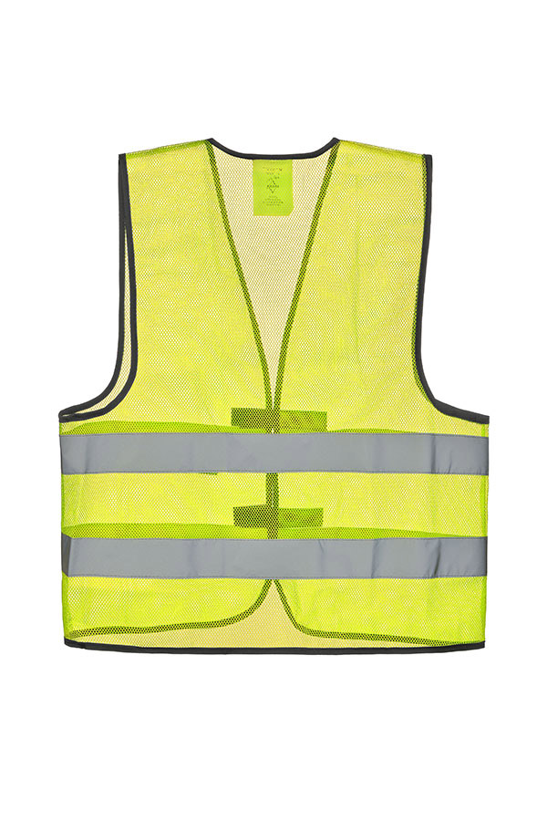 Adult construction worker stands on a building site in a yellow Korntex mesh safety vest and yellow helmet holding tools