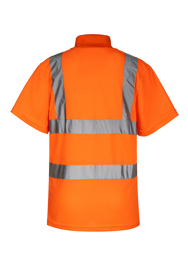 An adult construction worker is standing in front of a demolished building, wearing a fluorescent yellow Korntex polo shirt with a walkie-talkie.