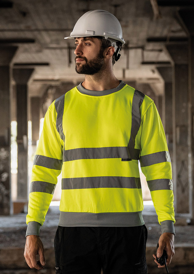 Adult man wearing a signal yellow Korntex Hi-Vis sweatshirt and white helmet on a construction site