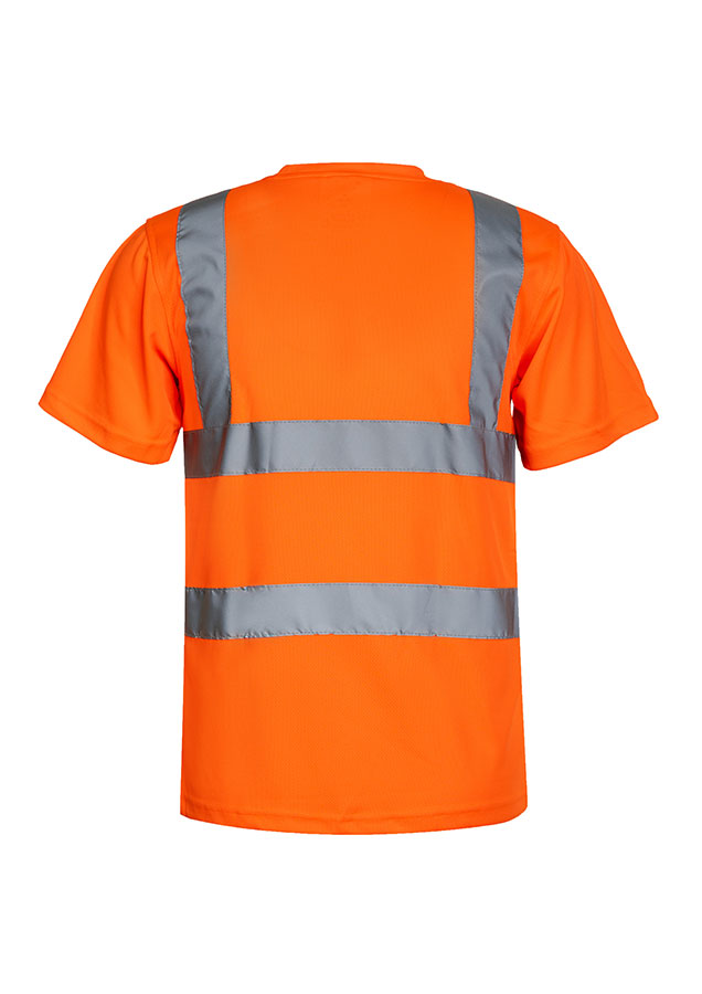 A woman, wearing a signal orange Korntex high-visibility T-shirt and a white hard hat, stands in front of scaffolding at an industrial construction site.