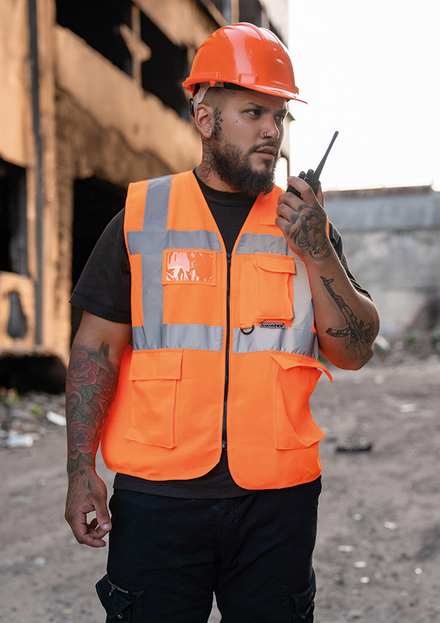 Construction worker in orange Korntex multifunctional safety vest and helmet communicates via radio on a construction site