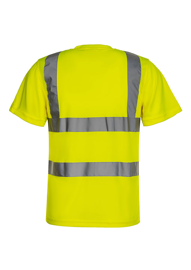 A woman, wearing a signal orange Korntex high-visibility T-shirt and a white hard hat, stands in front of scaffolding at an industrial construction site.