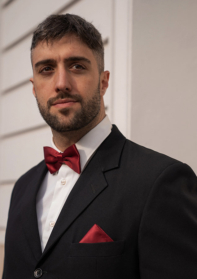 Portrait of an elegant man in a black suit and a Korntex bow tie in front of a building